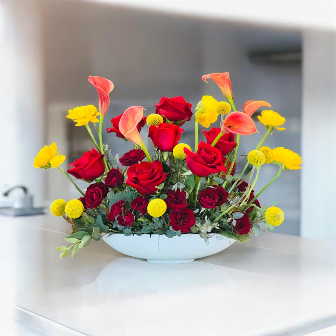 Red roses and yellow calla lilies arranged in a white bowl vase