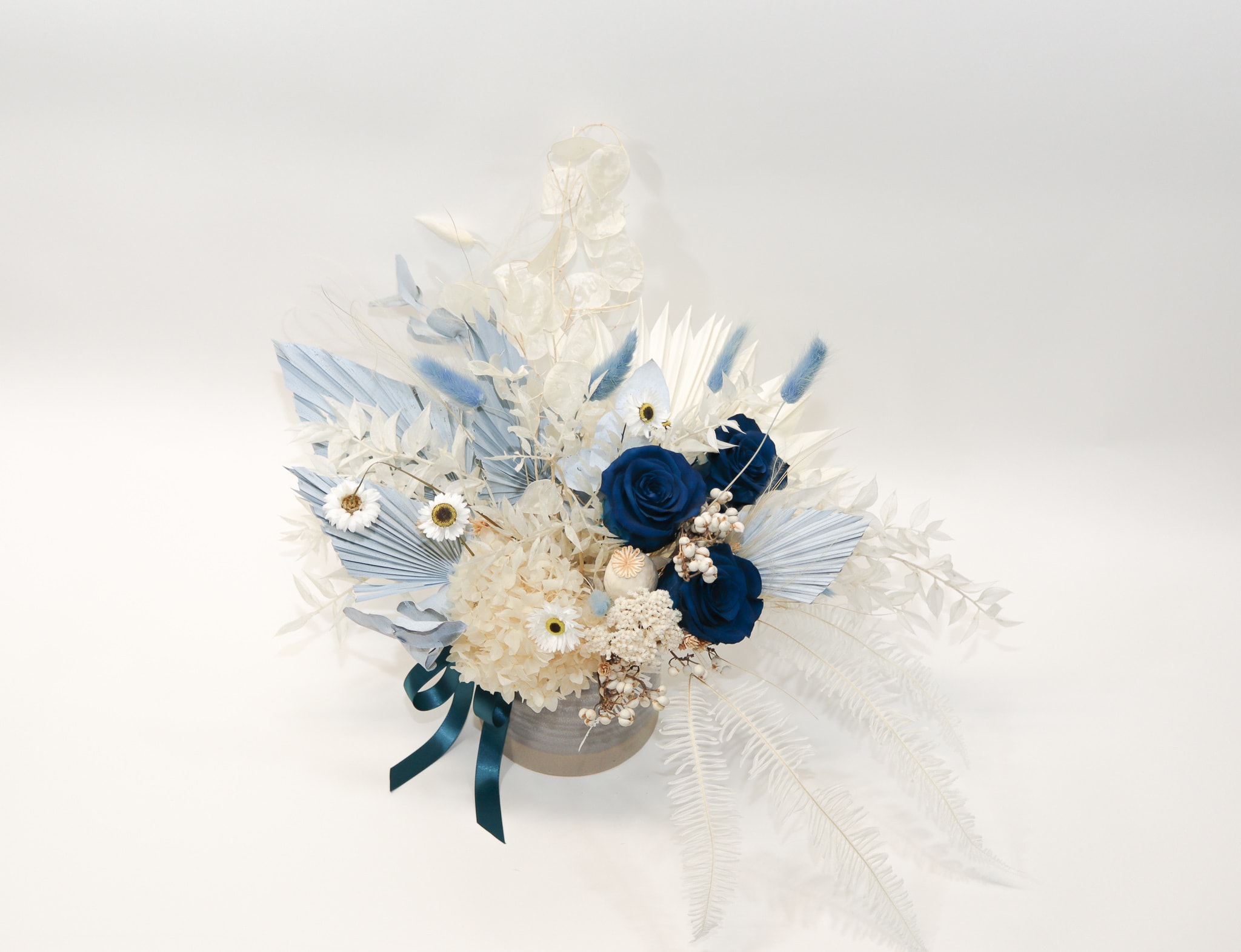 Blue and white floral arrangement in a round container with ribbon