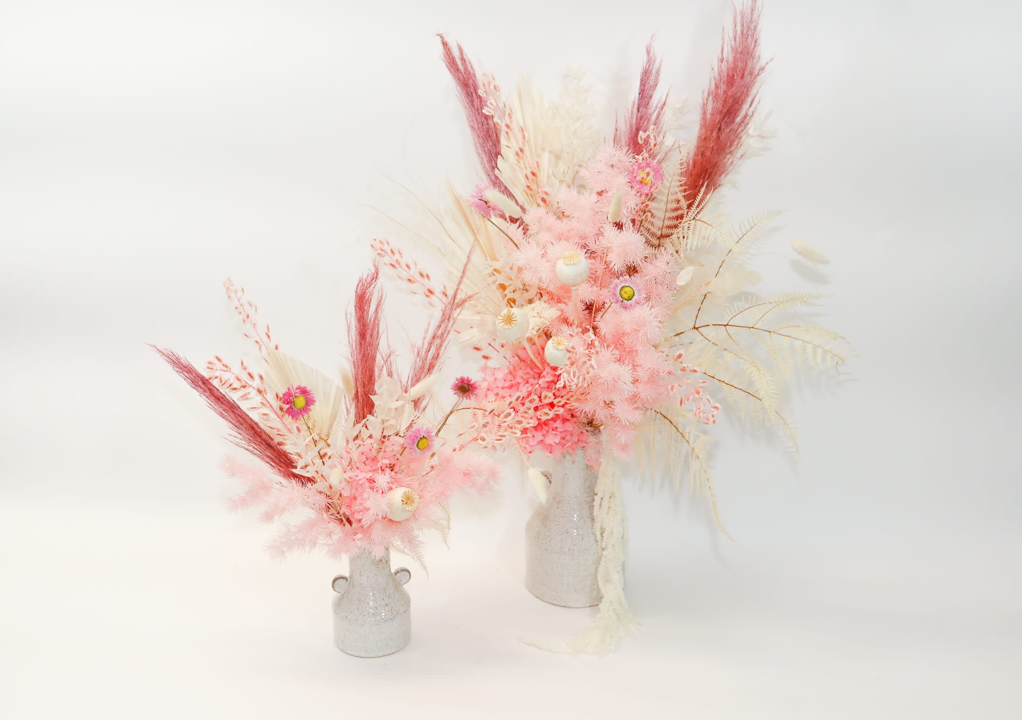 Two pink and white dried floral arrangements in small vases