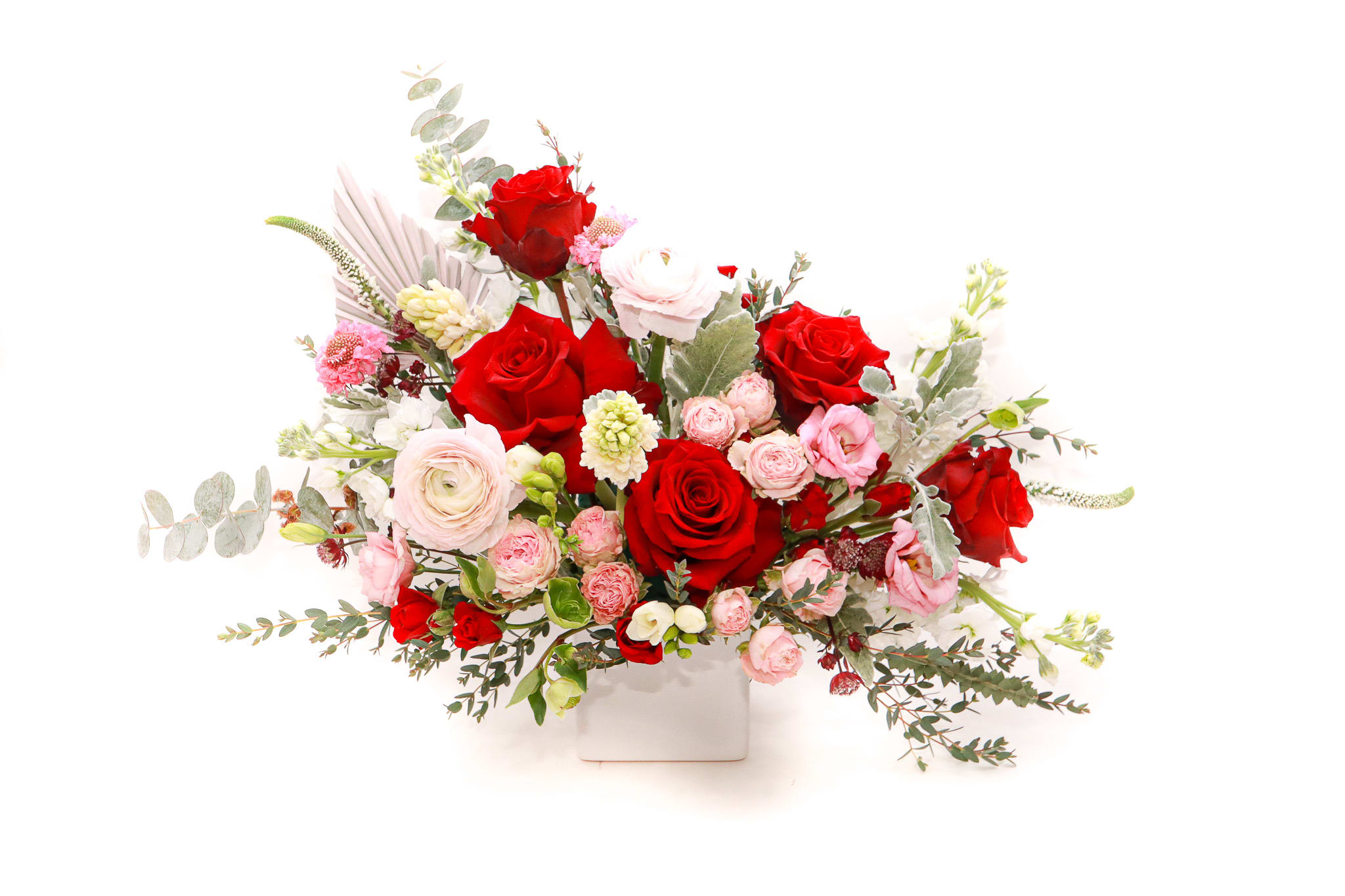 Red and pink rose arrangement in a white square vase