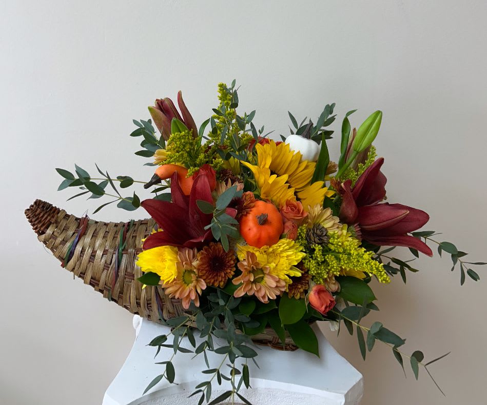 Cornucopia basket arrangement with red lilies, yellow blooms, and pumpkins