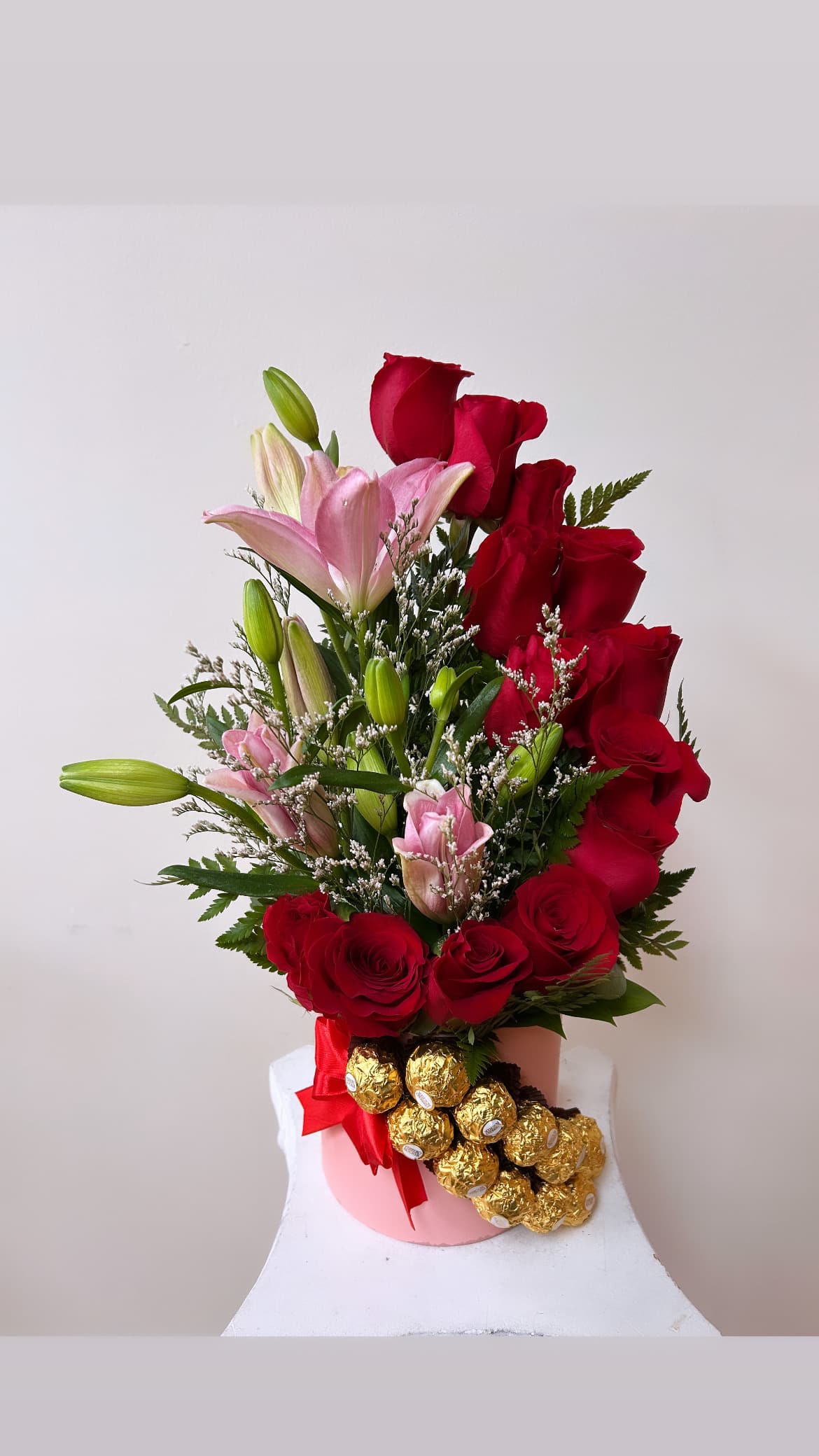 Red roses and pink lilies in a pink vase with gold-wrapped chocolates
