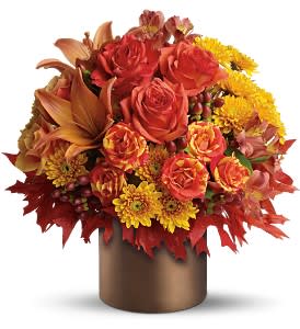 Autumn arrangement of orange roses, lilies, and yellow mums in a bronze cylinder vase