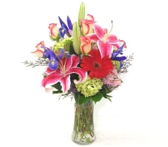 Mixed bouquet of lilies, roses, irises, and a red gerbera in a glass vase