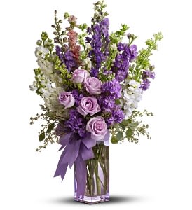 Lavender roses and purple stock in a clear square vase with a purple ribbon