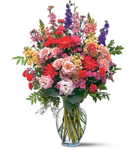 Tall mixed bouquet of pink, red, purple, and yellow flowers in a glass vase