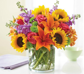 Bouquet of sunflowers, orange lilies, red roses, and purple flowers in a glass vase