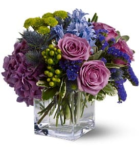 Purple and blue mixed bouquet in a clear square vase