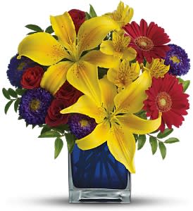 Bouquet of yellow lilies, red roses, and purple daisies in a blue vase