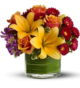 Bouquet of yellow lilies, orange roses, and red daisies in a glass vase