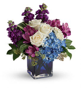 Bouquet of white roses, blue hydrangea, and purple flowers in a glass vase