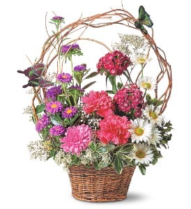 Basket arrangement of pink carnations, purple asters, and white daisies with a twig arch and butterflies.