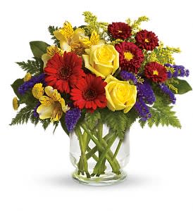 Mixed bouquet of yellow roses, red daisies, and purple filler in a glass vase