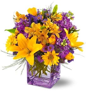 Purple and yellow mixed flower bouquet in a square glass vase