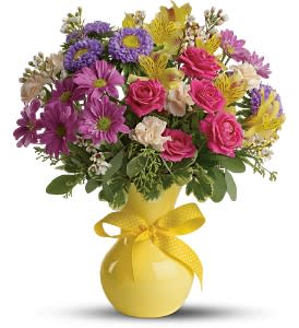 Mixed bouquet of pink, purple, and yellow flowers in a yellow vase with a ribbon
