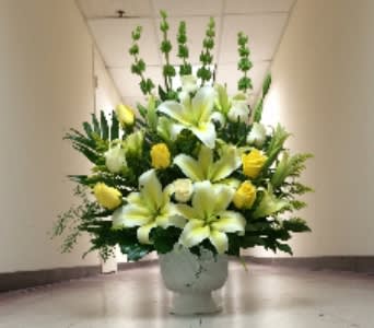 Tall yellow and white lily and rose arrangement in a white urn-style vase