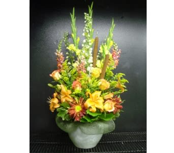 Tall autumn-toned arrangement with orange lilies, roses, and cattails in a frosted vase