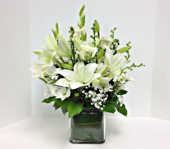 White lilies arranged in a square glass vase with greenery