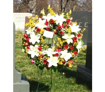 Standing wreath of white lilies, red roses, and yellow flowers on an easel in a cemetery.
