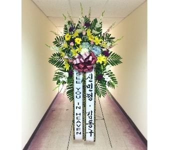 Tall standing funeral spray with yellow lilies, mixed blooms, and message ribbons on an easel