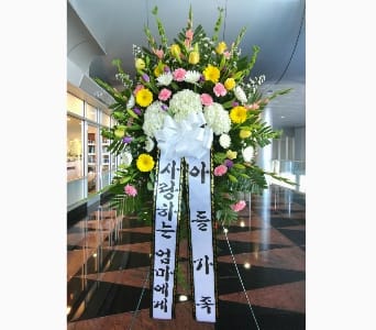Tall standing sympathy spray with yellow, pink, and white flowers and Korean message ribbons on an easel
