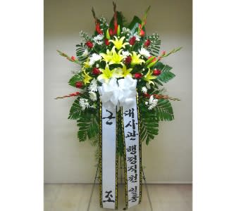 Tall standing spray with yellow lilies, red roses, white flowers, and long message ribbons in Korean.
