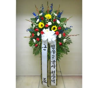 Tall standing spray with yellow sunflowers, red carnations, and white flowers on an easel