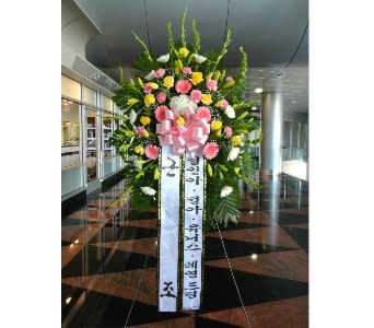 Tall standing spray of pink, yellow, and white flowers with a large pink bow and Korean message ribbons
