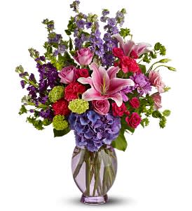 Mixed bouquet with pink lilies, roses, hydrangea, and purple flowers in a glass vase