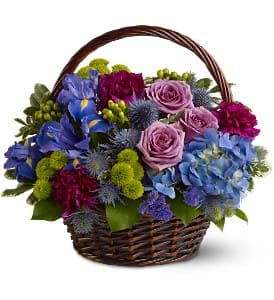 Basket arrangement of blue hydrangeas, purple roses, blue irises, and green button mums