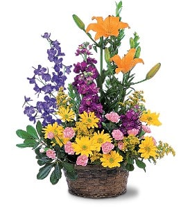 Basket arrangement with orange lilies, purple flowers, yellow daisies, and pink blooms.