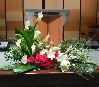 Large red and white floral spray with calla lilies, roses, and lilies arranged in front of a podium