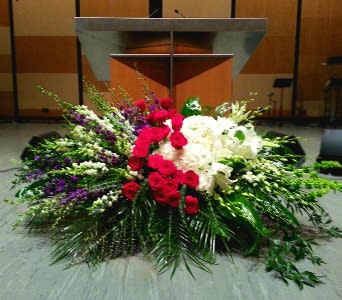 Large red, white, and purple floral spray with roses and lilies arranged in front of a podium.
