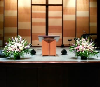Two large pink, white, and purple altar arrangements flanking a wooden podium on a stage