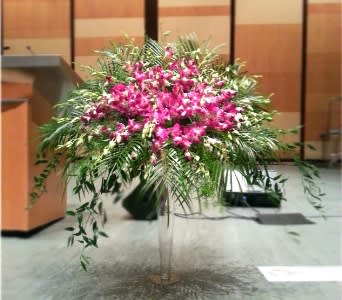 Large pink orchid arrangement with cascading greenery on a clear pedestal stand indoors