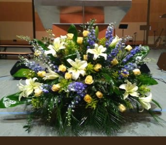 Large altar arrangement with white lilies, yellow roses, and purple flowers in a fan-shaped design