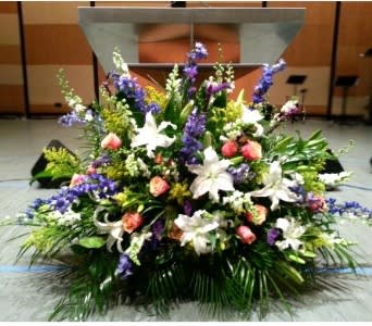 Large altar arrangement with white lilies, peach roses, and purple flowers on a stage