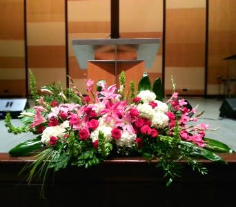 Low altar floral arrangement with pink lilies, red roses, and white blooms in front of a podium