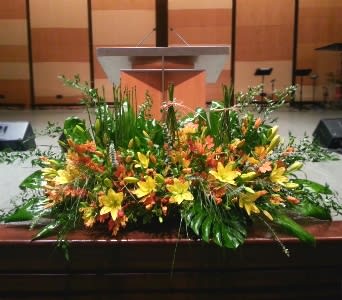 Large yellow and orange floral arrangement with lilies in front of a wooden podium