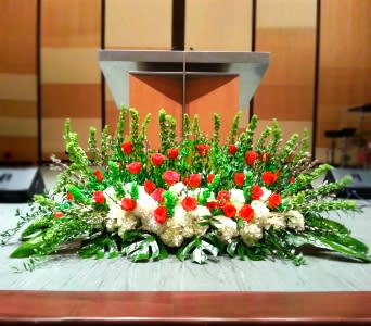 Large altar spray with red roses, white hydrangeas, and tall green spikes in front of a podium
