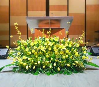 Large low arrangement of yellow lilies and tulips displayed on a stage in front of a podium