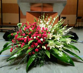 Large red carnation and white lily stage arrangement with abundant foliage in front of a podium