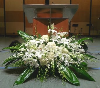 Large white lily and mum arrangement displayed in front of a wooden podium