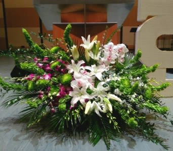 Large white lily and orchid floor arrangement with green accents in front of a stage