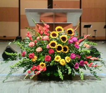 Large stage arrangement of yellow sunflowers with pink and orange flowers in front of a podium