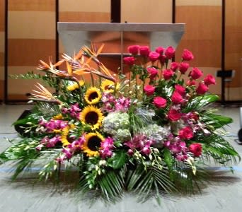 Large altar arrangement with pink roses, sunflowers, birds of paradise, orchids, and hydrangeas in a fan shape