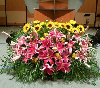 Large stage arrangement of pink lilies, yellow sunflowers, and yellow blooms in a low, wide design