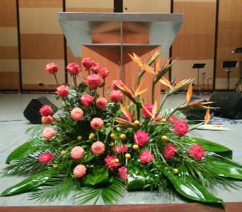 Large stage arrangement with pink roses, round pink blooms and orange tropical flowers in front of a podium