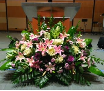 Large mixed arrangement of pink lilies and cream blooms displayed in front of a podium.