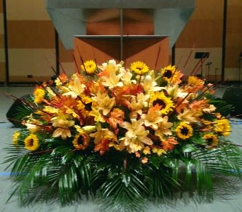 Large low altar-style arrangement of yellow lilies and sunflowers with orange blooms and palm fronds